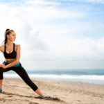 young-woman-stretching-legs-on-sandy-beach-in-the-morning